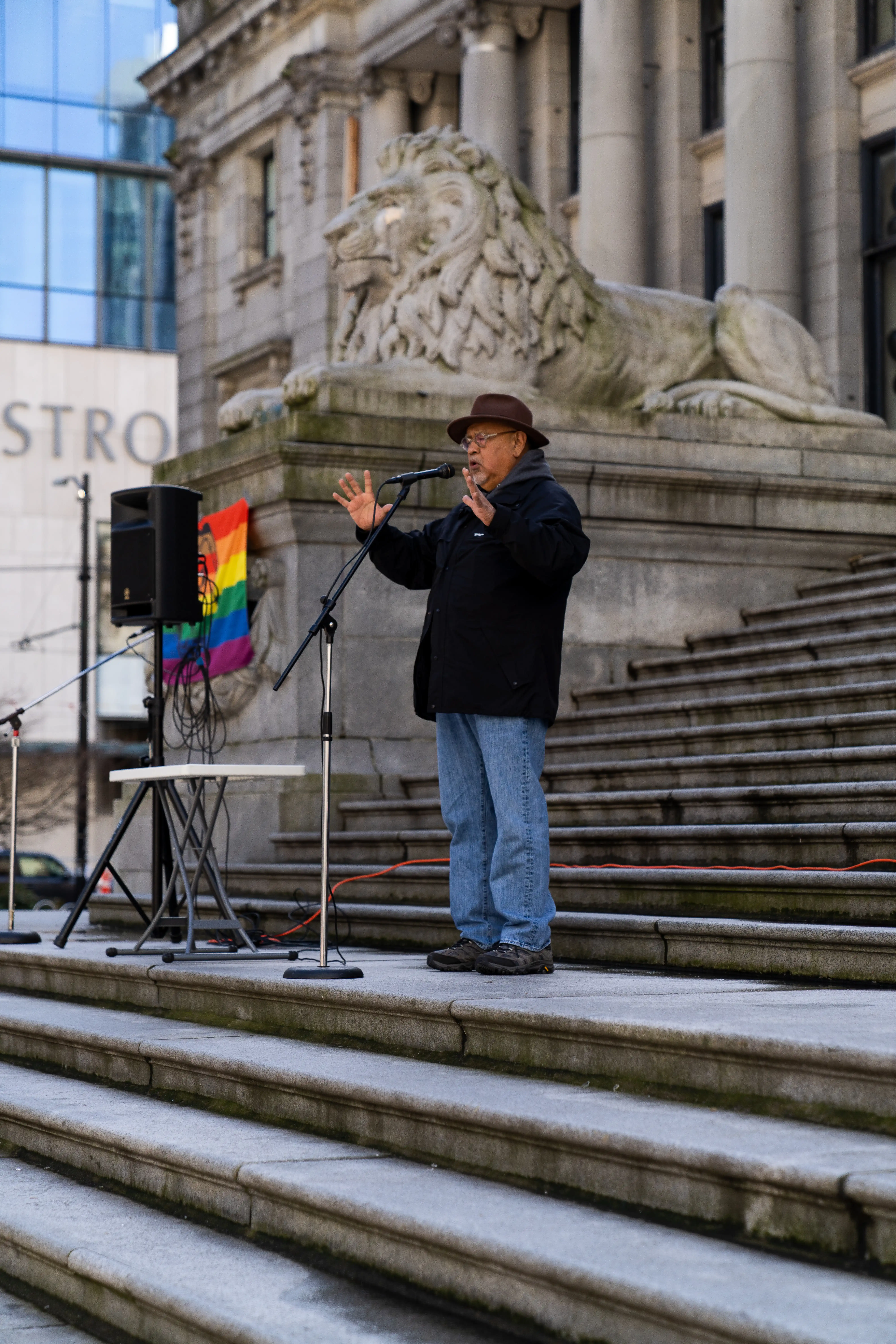 This is an image of Elder Shane, speaking to the crowd. He is speaking into a microphone on large stone stairs outside.