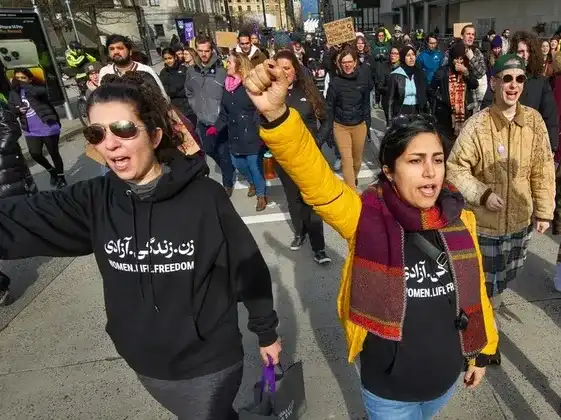 This image is a hyperlink to a news article by Vancouver Sun. The image contains event participants marching on a Vancouver street. Their fists are raised in solidarity. 